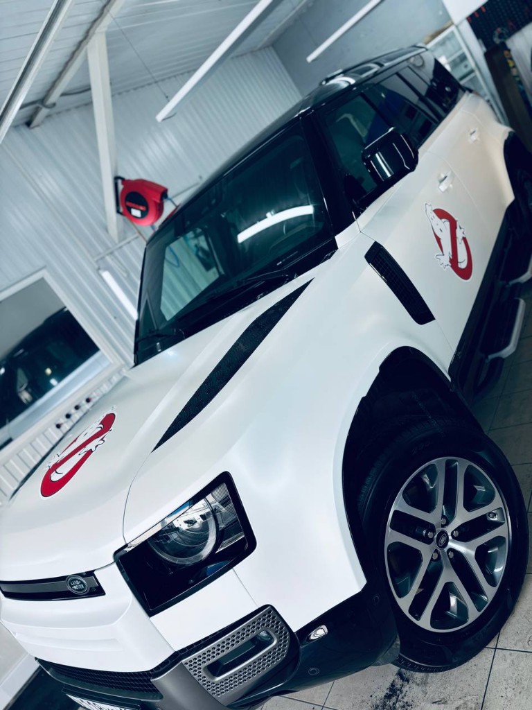 Land Rover Defender в белом сатине SKINGARD — передний 3/4 с логотипом Ghostbusters